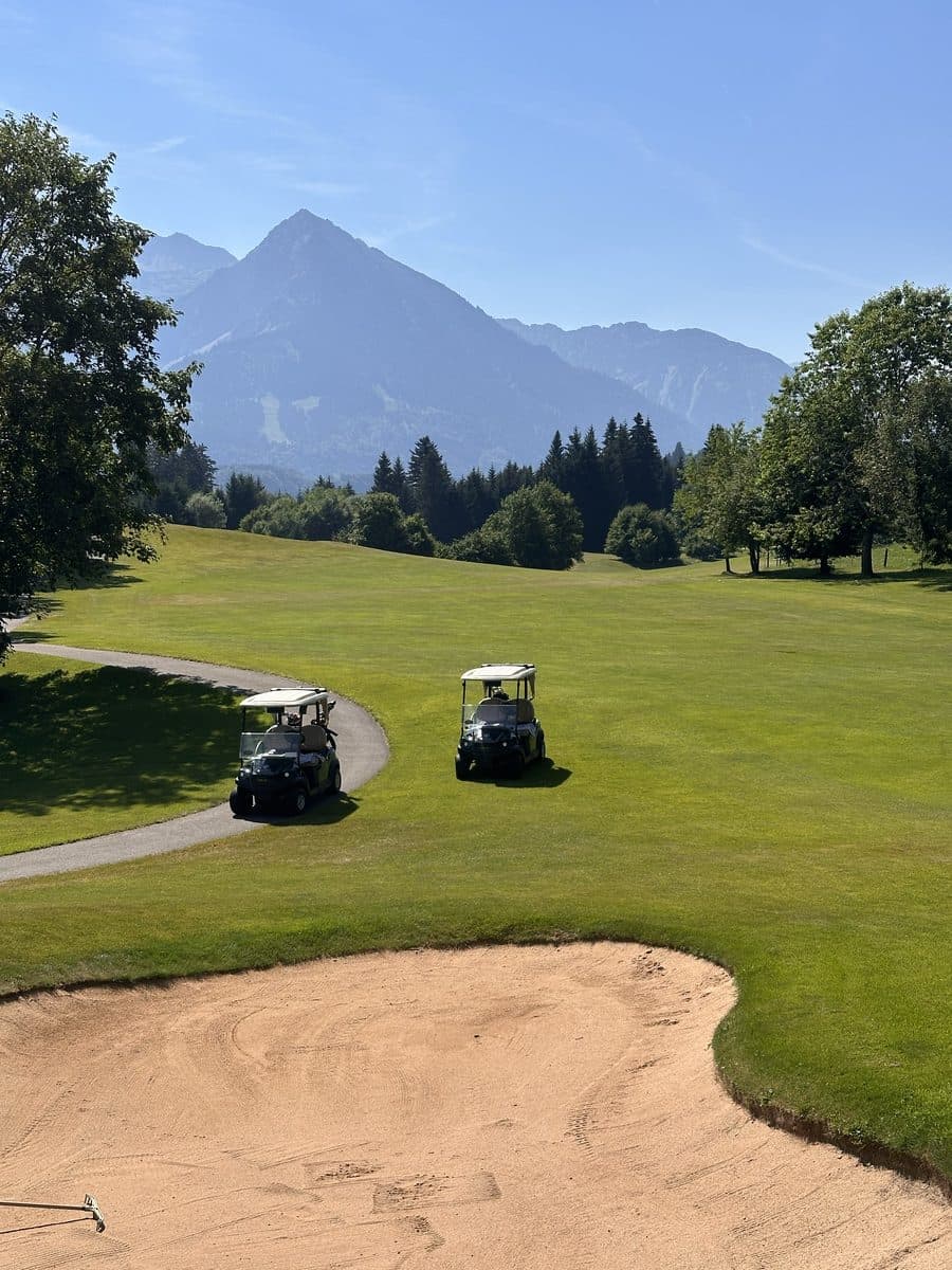 Fairway with a sand bunker, two golf carts and mountains behind