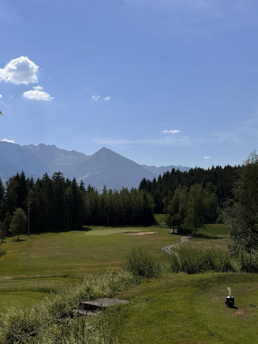 Golf course between forest and mountains under a blue sky